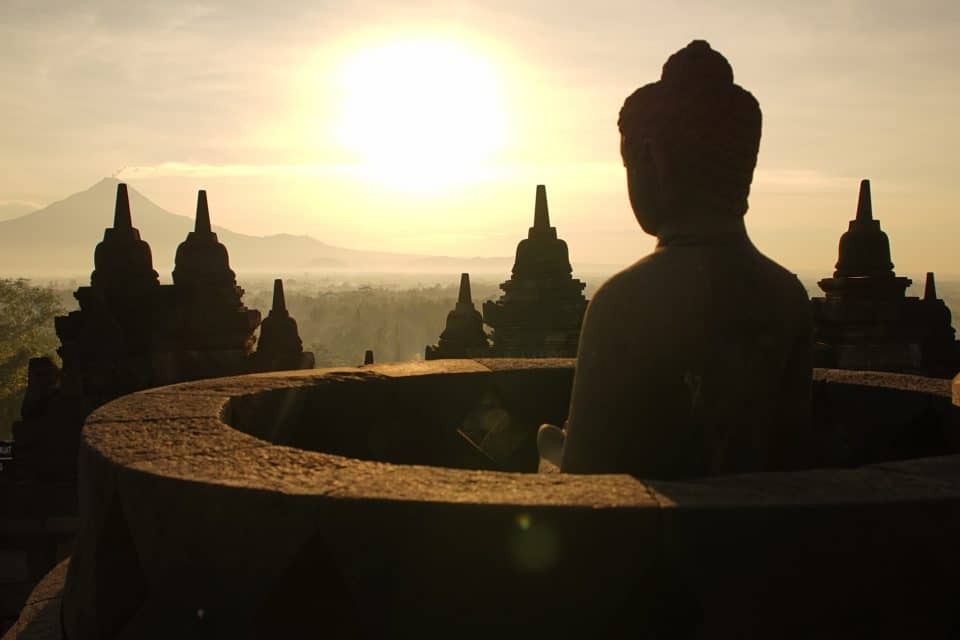 The sun rises in front of one of the many budda statues at Borobudur, Yogyakarta, Indonesia