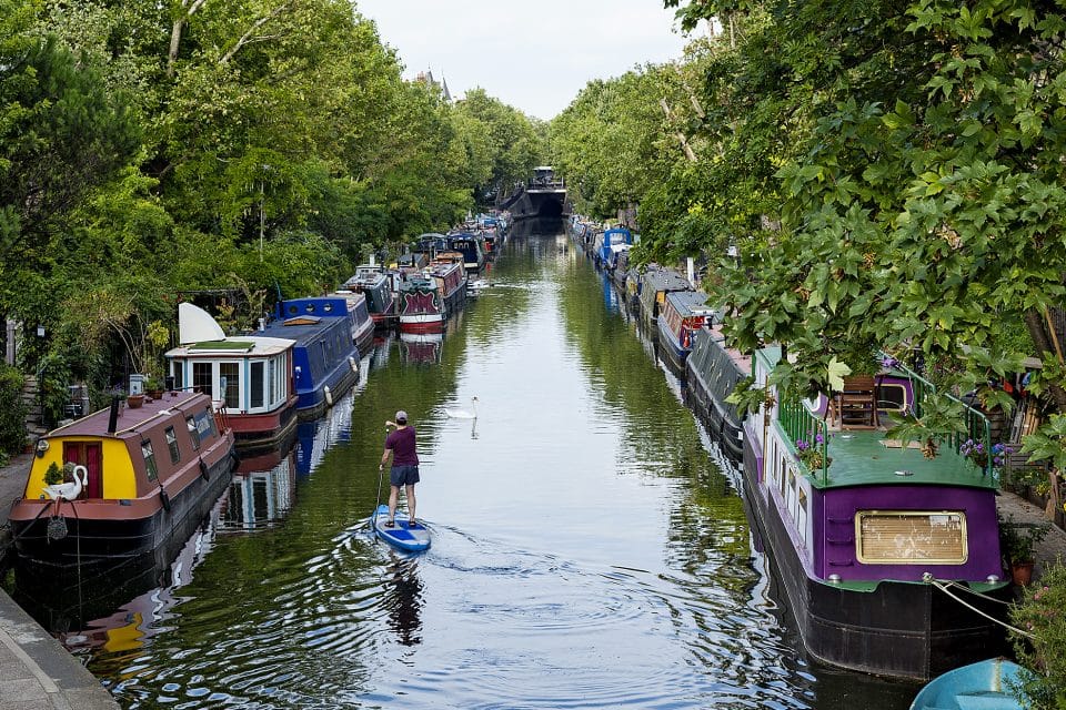 A man paddle boarding down a canal