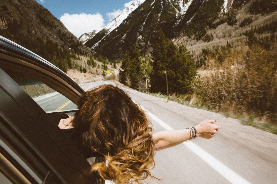 Woman hanging out the window of a driving car