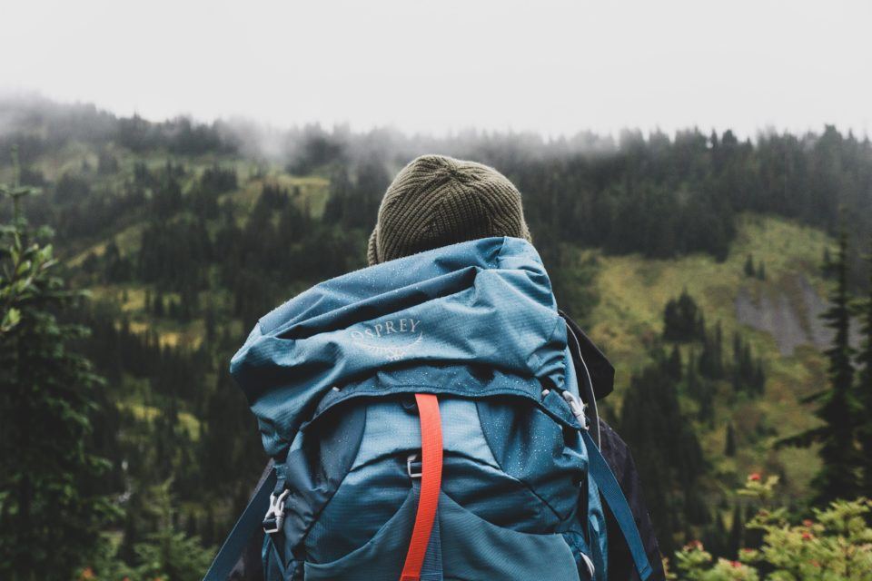person standing among trees with osprey backpack