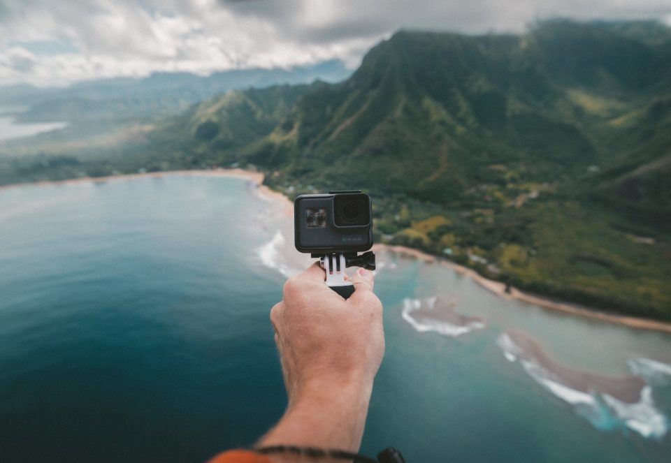 person holding a gopro in front of mountains and water