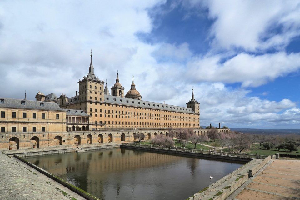 giant building in front of pool of water and blue sky with clouds
