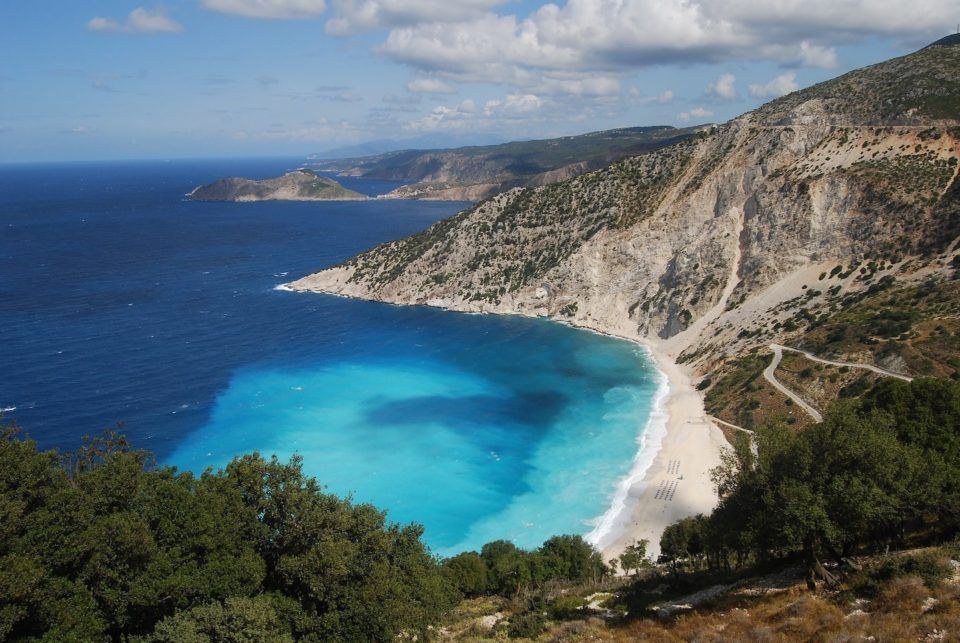 Aerial view of beach surrounded by mountains and dark blue water that's light near the shore.