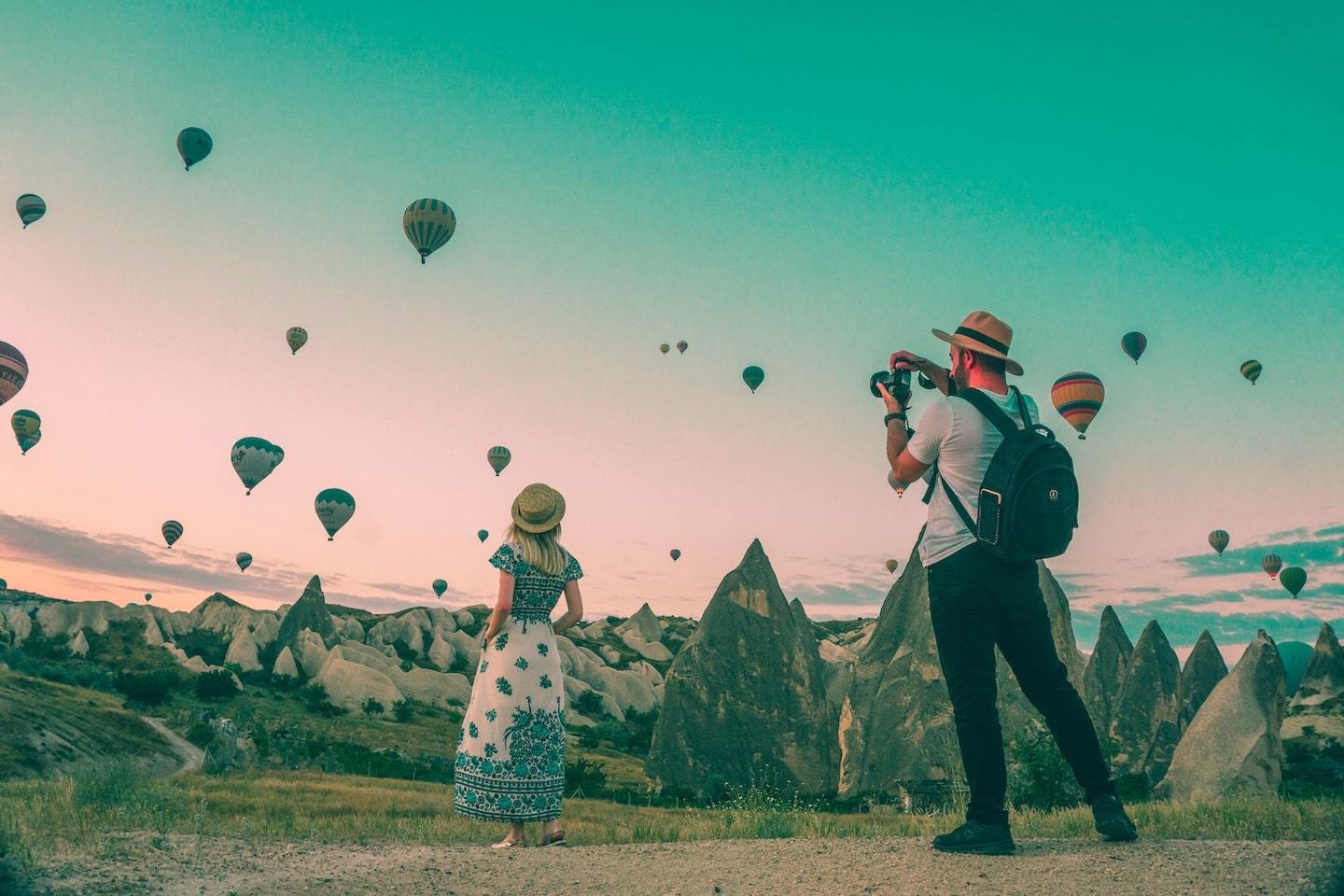 man taking picture of a woman with hot air balloons in the back
