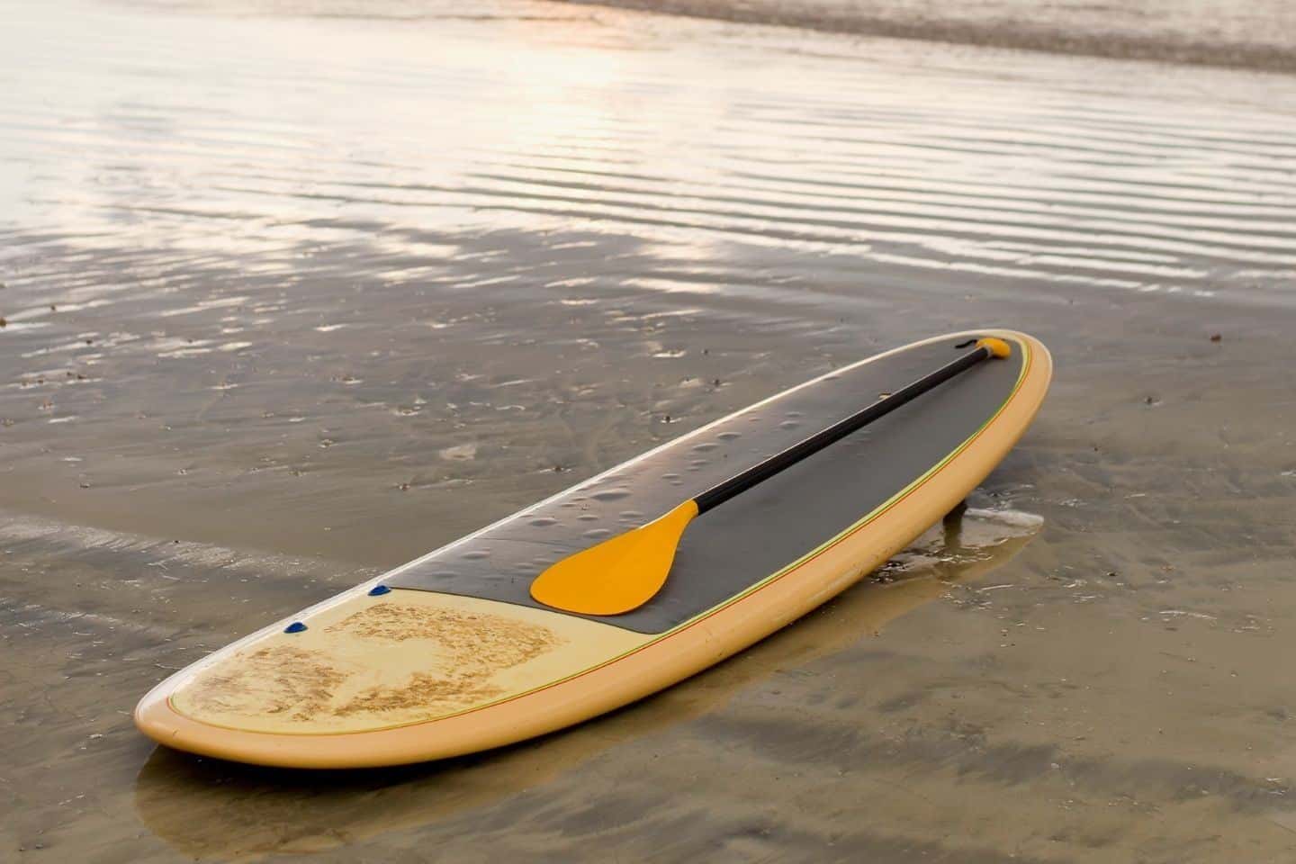 A yellow paddle board and oar on a tropical beach